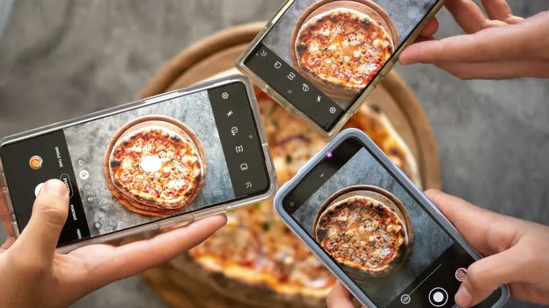 Three people taking a photo of a pizza